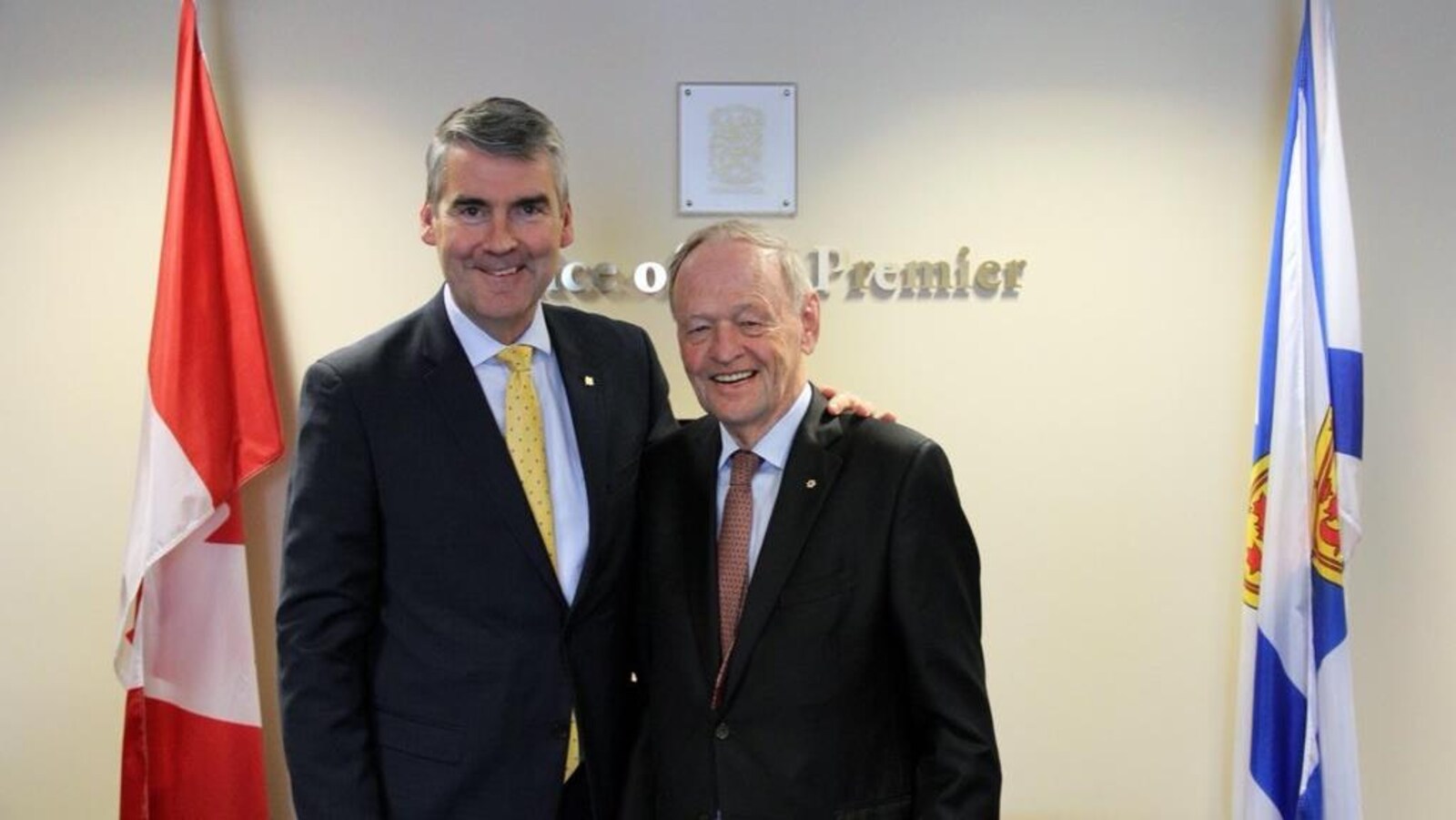 Jean Chrétien et Stephen McNeil côte à côte devant les drapeaux du Canada et de la Nouvelle-Écosse.