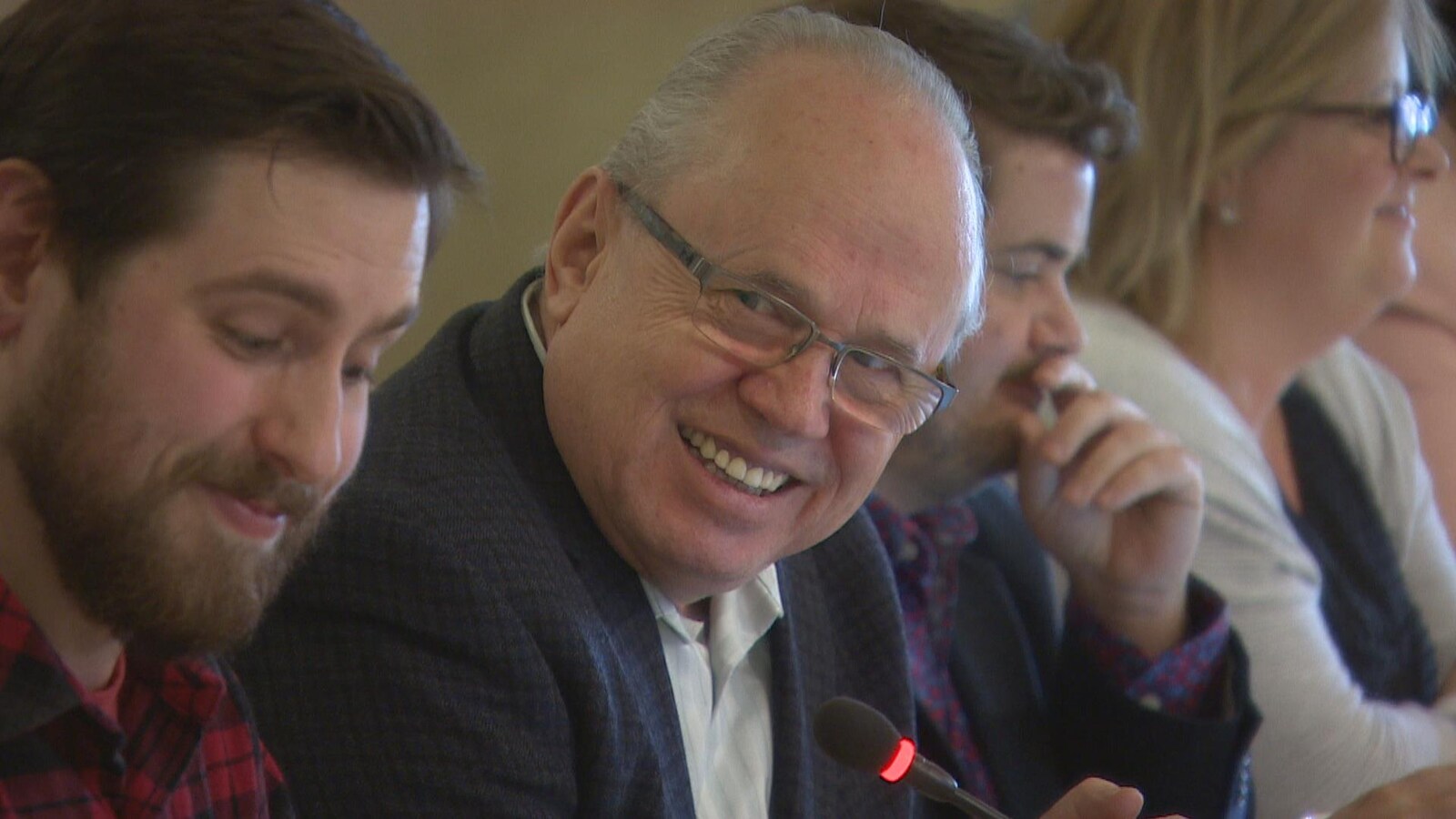 Gros plan sur Jean Johnson, au centre, un homme à lunettes souriant, aux côtés d'autres membres de la FCFA, assis dans une salle de conférence.