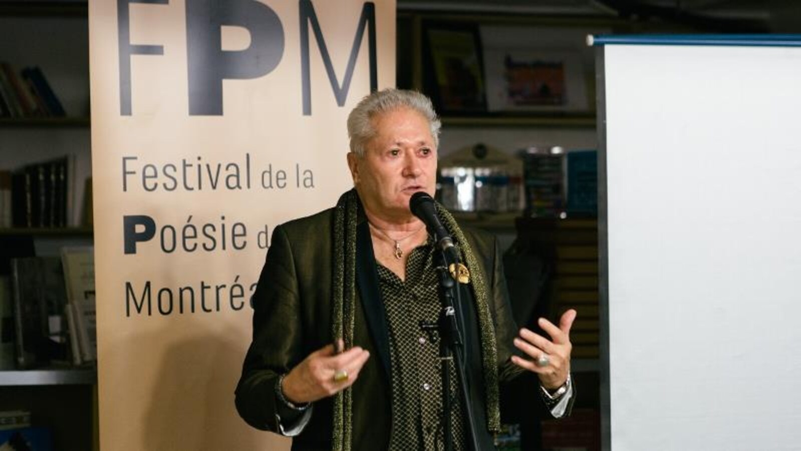 Le poète se tient debout devant un micro et parle.