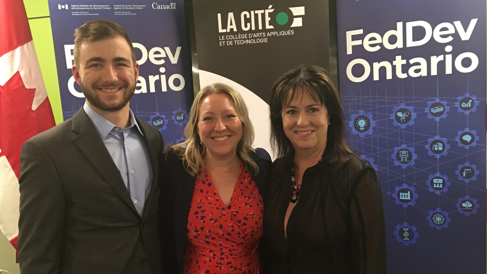 Jean-Philippe Héroux, entrepreneur (à gauche), Mona Fortier, députée fédérale d’Ottawa-Vanier (au milieu) et Lise Bourgeois, présidente-directrice générale de La Cité, sourient devant des panneaux FedDev et un drapeau canadien.