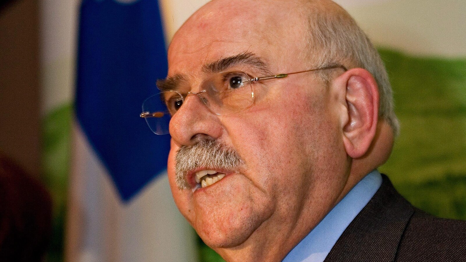 Un homme moustachu qui porte des lunettes s'exprime lors d'une conférence de presse.
