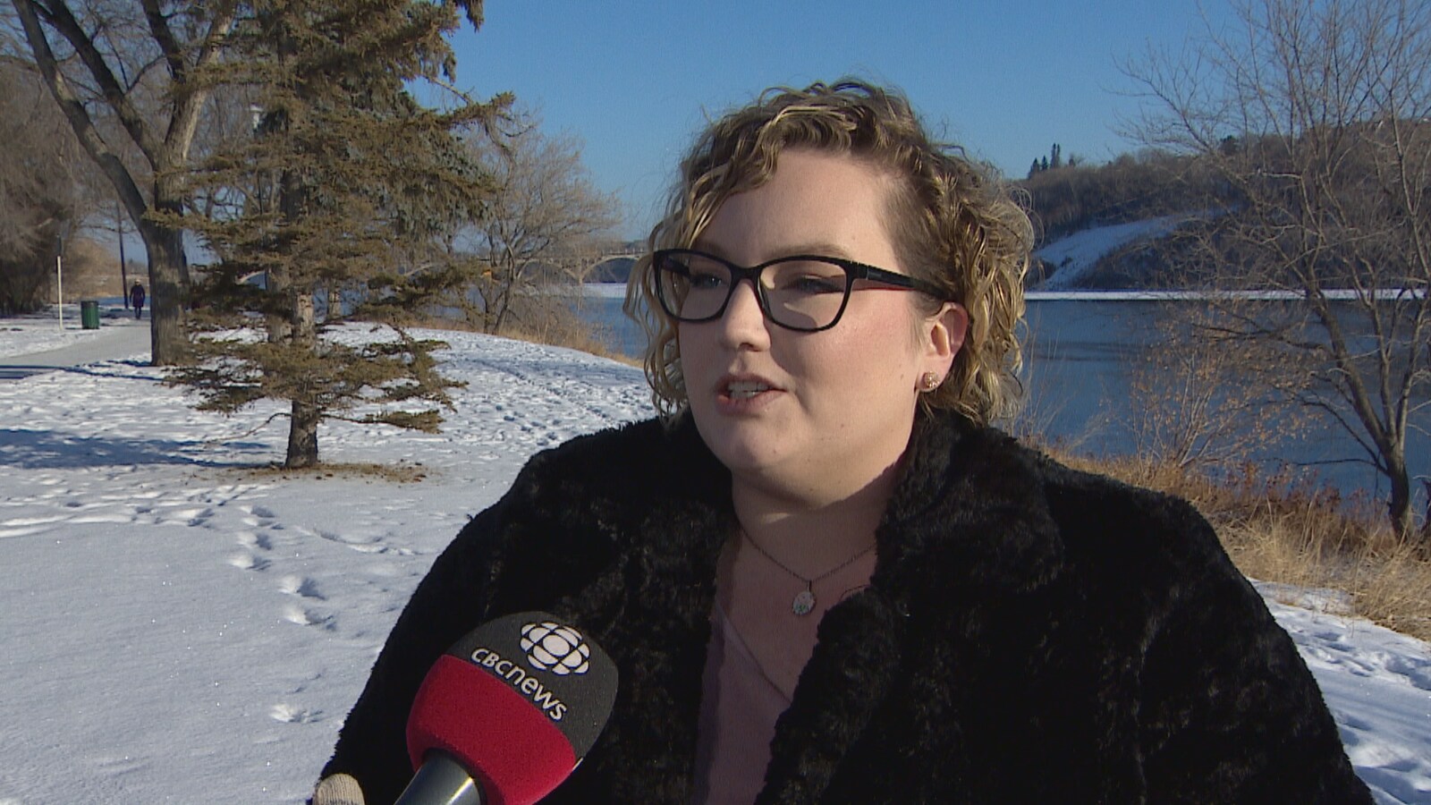 Une femme dans un décor hivernale, avec des lunettes et les cheveux clairs, elle parle devant un micro de CBC News