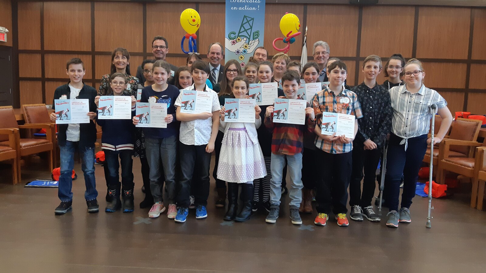 Des enfants tiennent fièrement des certificats, des adultes sourient aussi derrière eux.