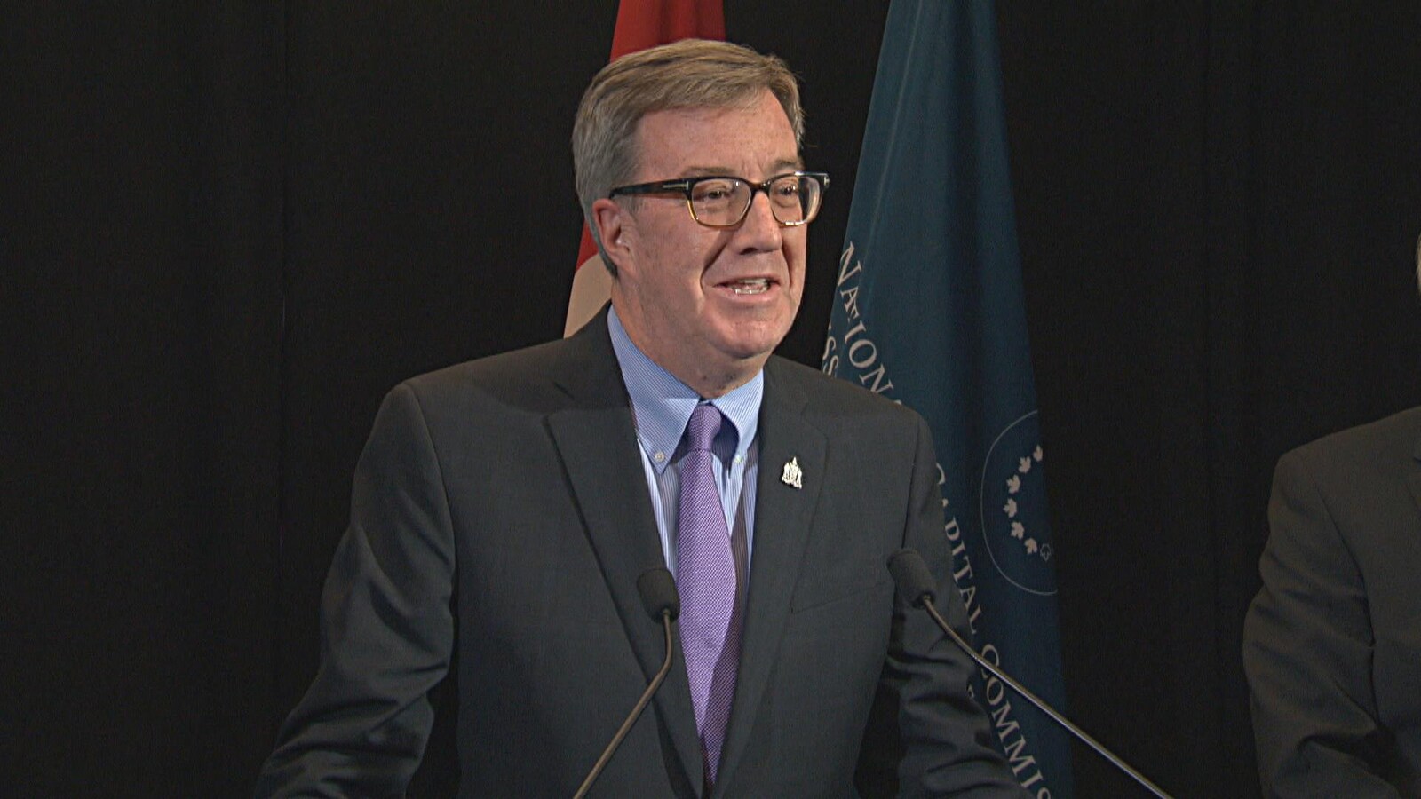 Le maire Jim Watson est debout devant un podium et sourit.