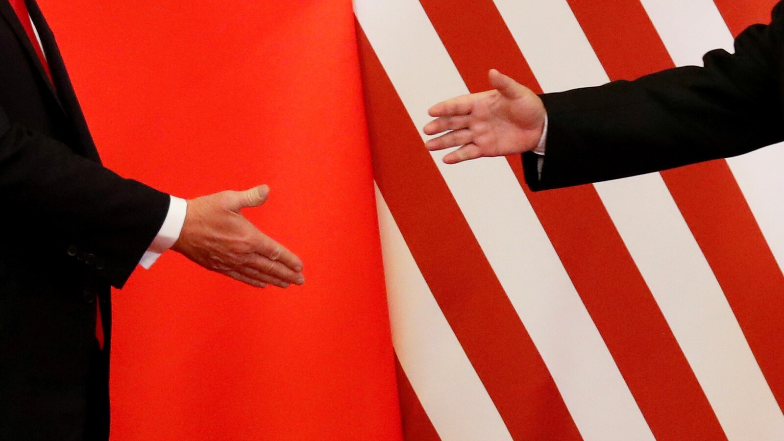 Devant les drapeaux chinois et américain tendus en fond de scène, gros plan de la main du président chinois et de celle du président américain, à quelques centimètres l’une de l’autre.