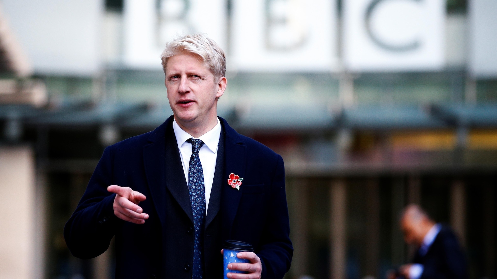 Jo Johnson quitte les bureaux de la BBC, café à la main.