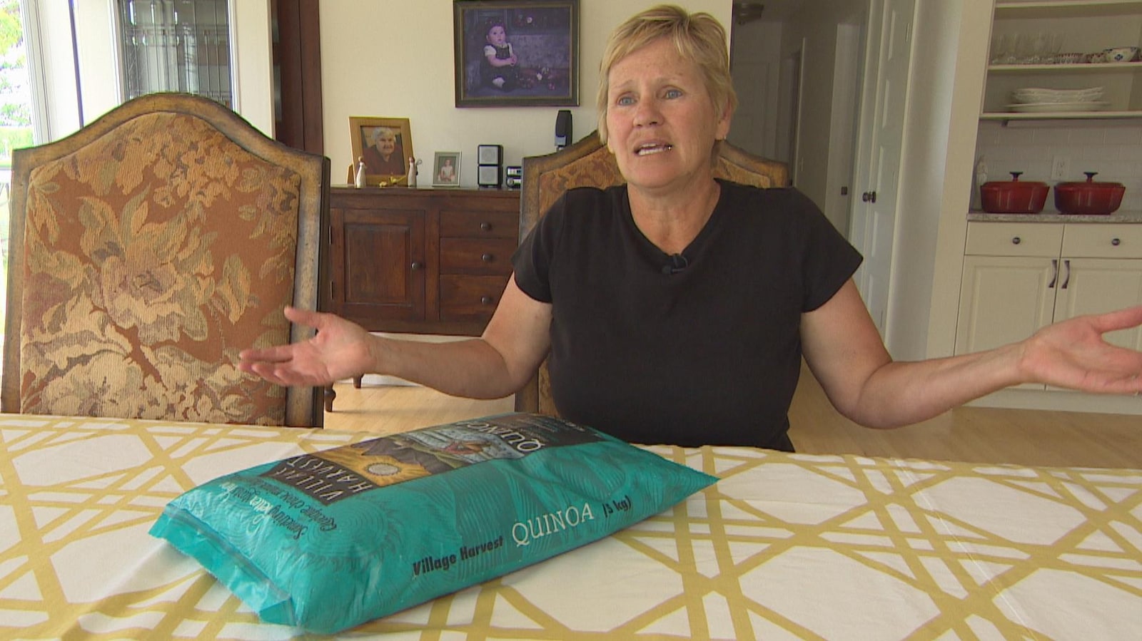 Une dame d'une cinquantaine d'années, avec des cheveux blonds coupés courts, lève les mains en signe d'impuissance devant un grand sac de quinoa posé sur sa table à manger.