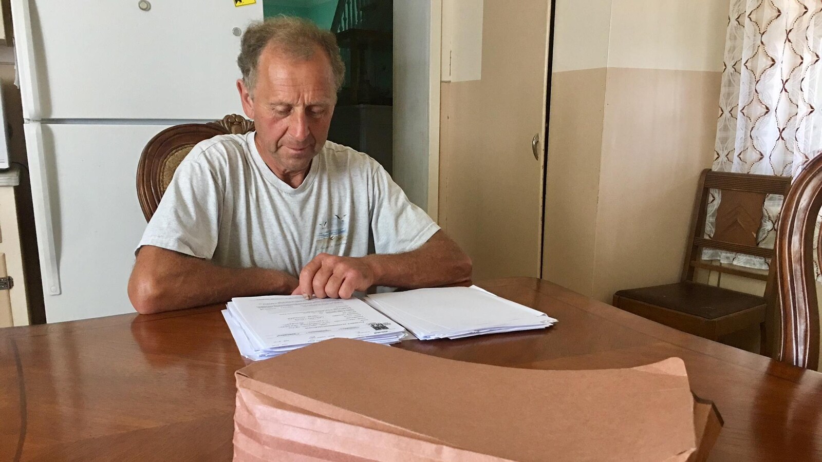 Un homme assis à une table de cuisine regarde une pile de papiers.