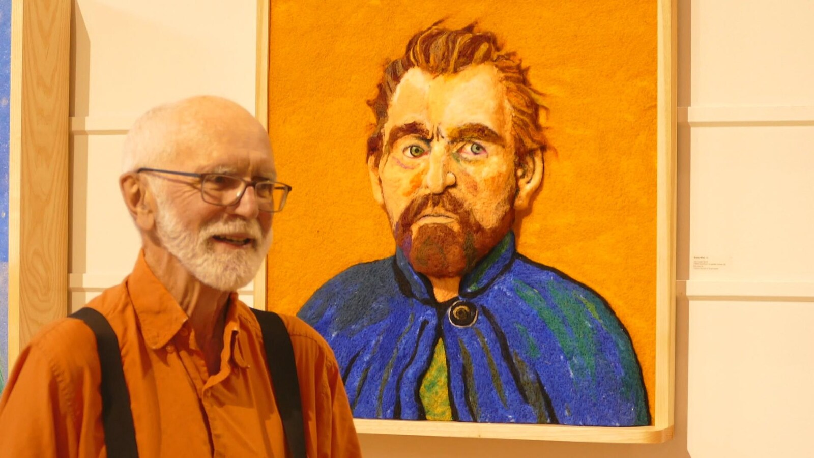 Un homme pose devant un portrait aux tonalités orange et bleue.