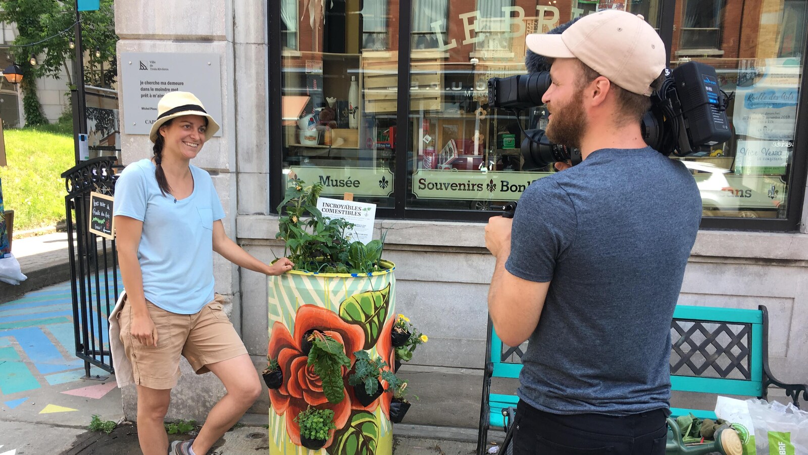 Appuyée contre un bac à légumes communautaire, Joëlle Carle s'adresse à une caméra tenue par un homme.
