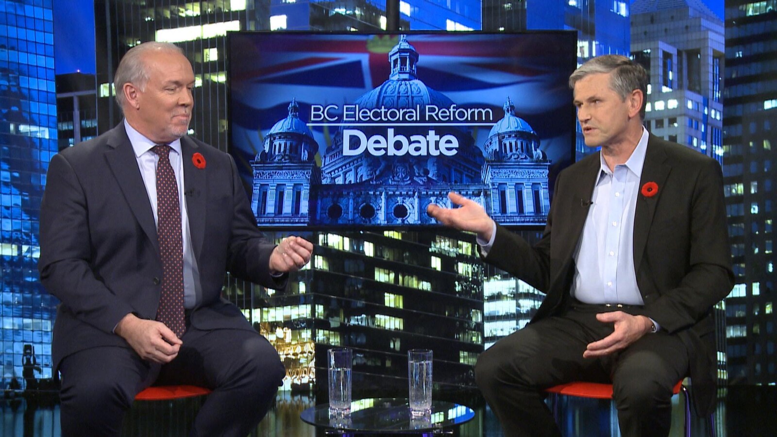John Horgan et Andrew Wilkinson assis devant un écran de télé où il est écrit en anglais, la réforme électorale de la Colombie-Britannique, débat.