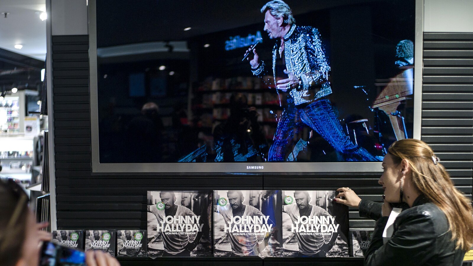 Une femme se fait photographier alors qu'elle est en train de prendre un disque de Johnny Hallyday sur un présentoir.