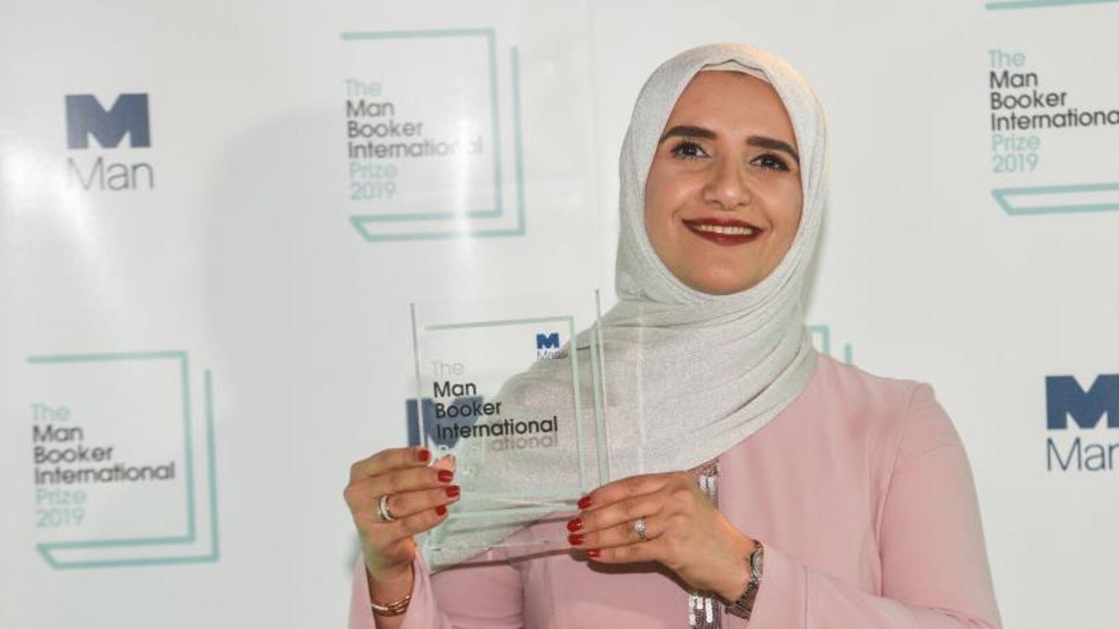 Jokha Alharthi souriant en tenant son prix (une plaque en vitre) entre ses mains.