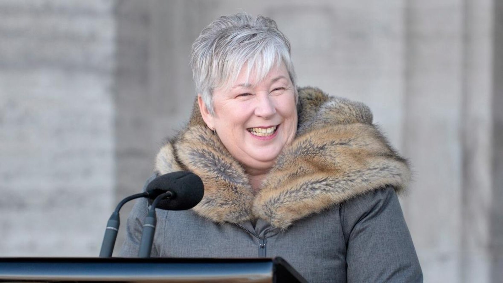 Bernadette Jordan, souriante, parle dans un micro installé devant l'édifice.