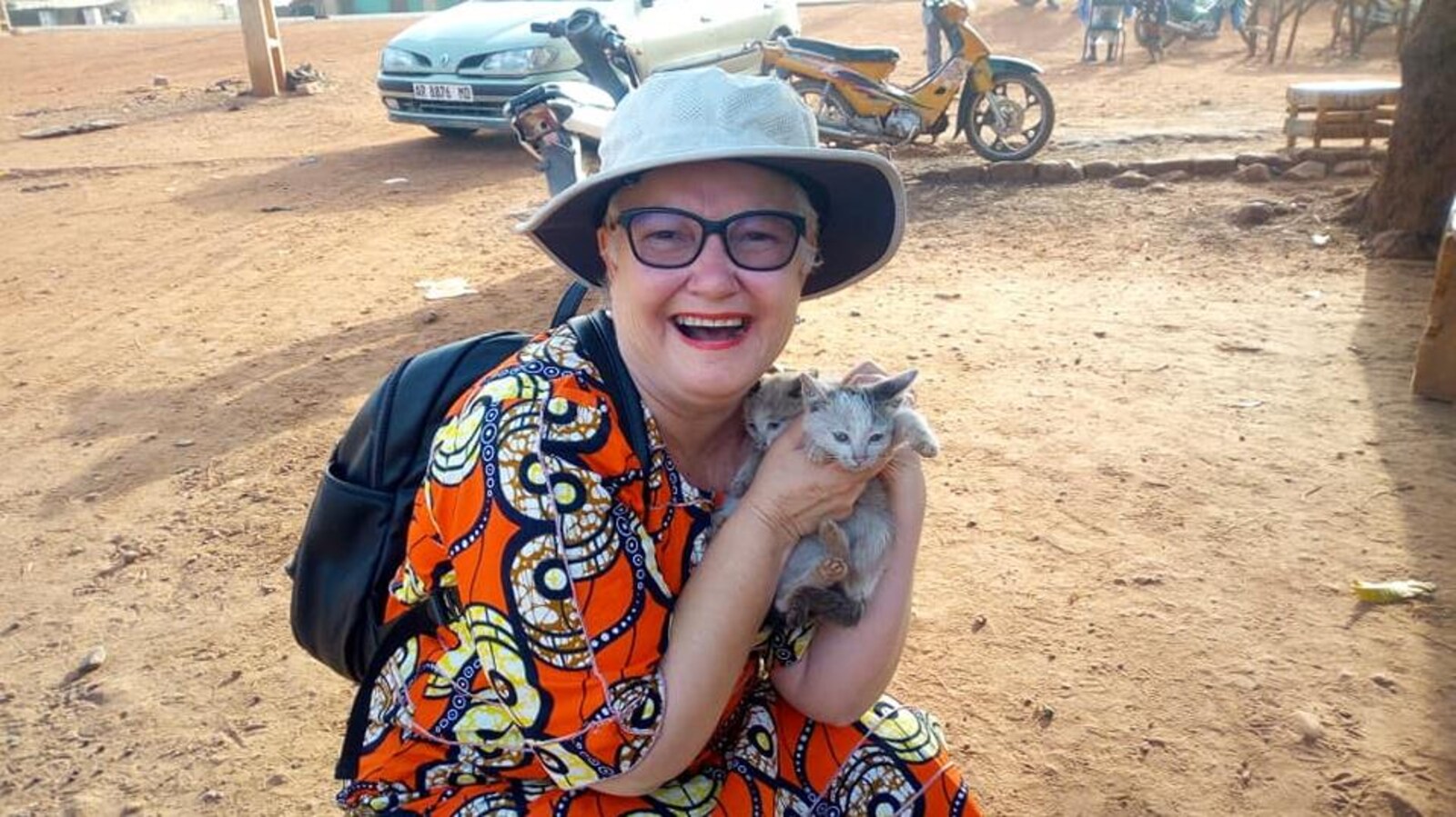 José Leclair, en boubou africain, tout sourire, tient des bébés chats dans ses mains.