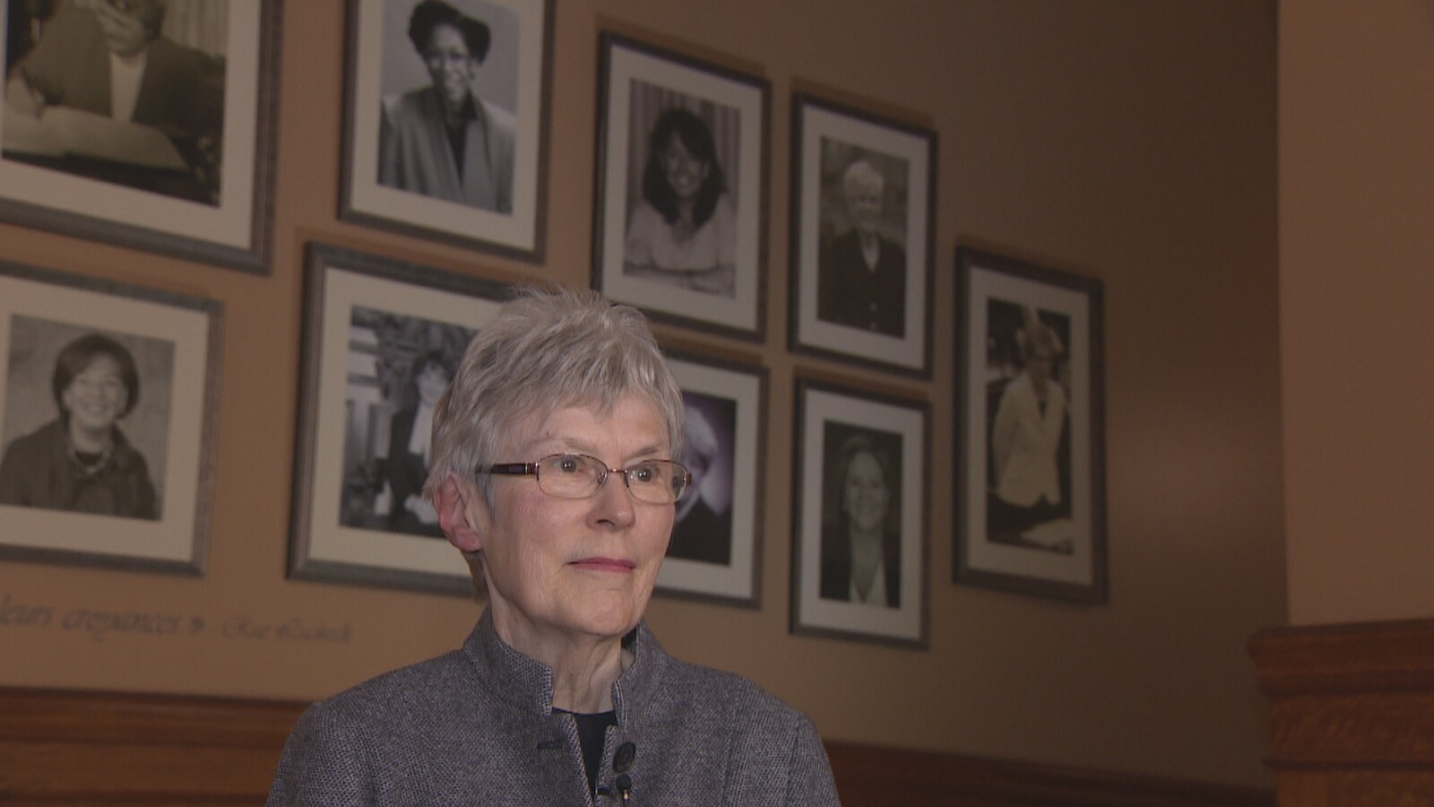 Julia Munro, debout, fait dos aux photos de femmes politiques influentes à l'Assemblée législative ontarienne.