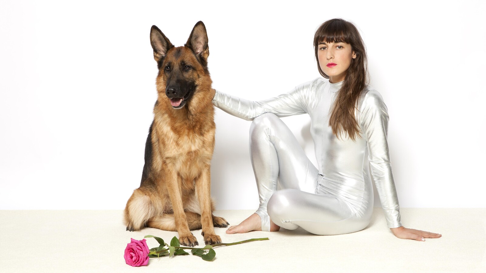 Juliette Armanet, vêtue d'une combinaison métallique, caresse d'un chien de race berger allemand durant une séance de photo promotionnelle.