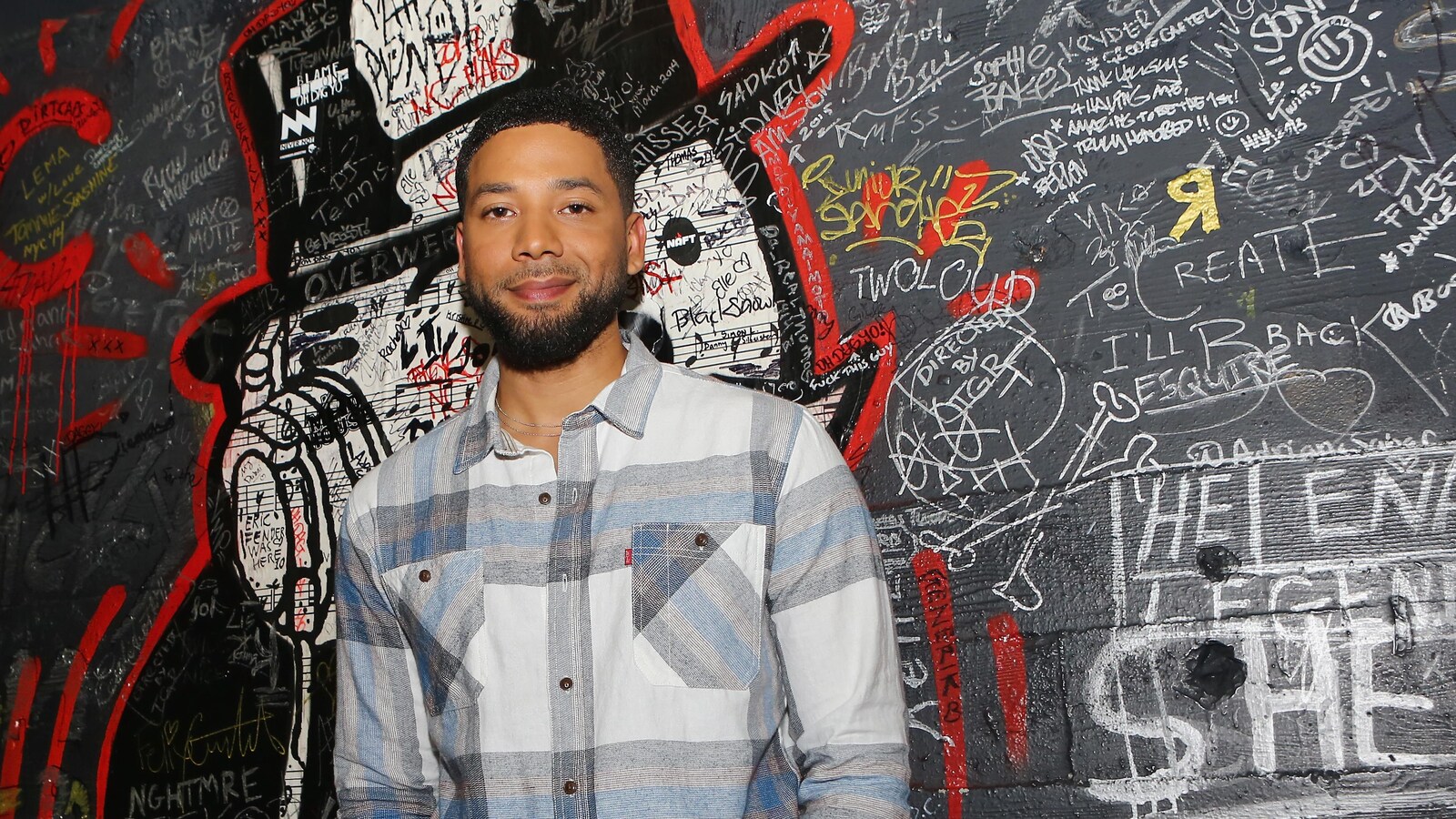 L'acteur Jussie Smollet pose devant un mur couvert de graffitis.