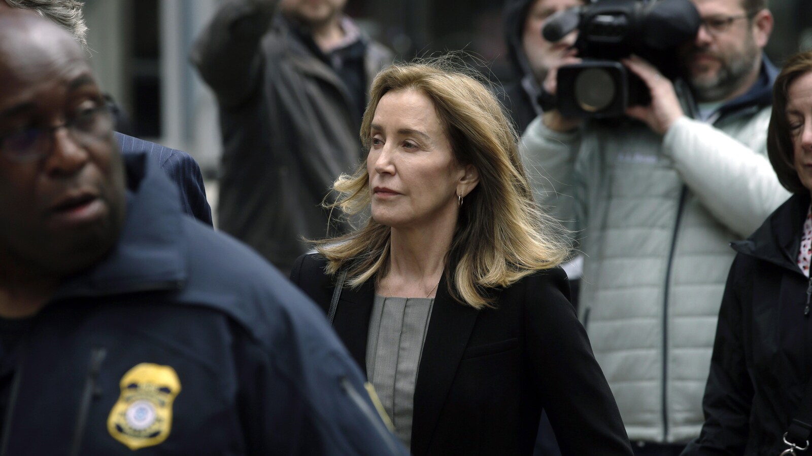 L'actrice Felicity Huffman marche, précédée d'un policier et suivie d'un caméraman.