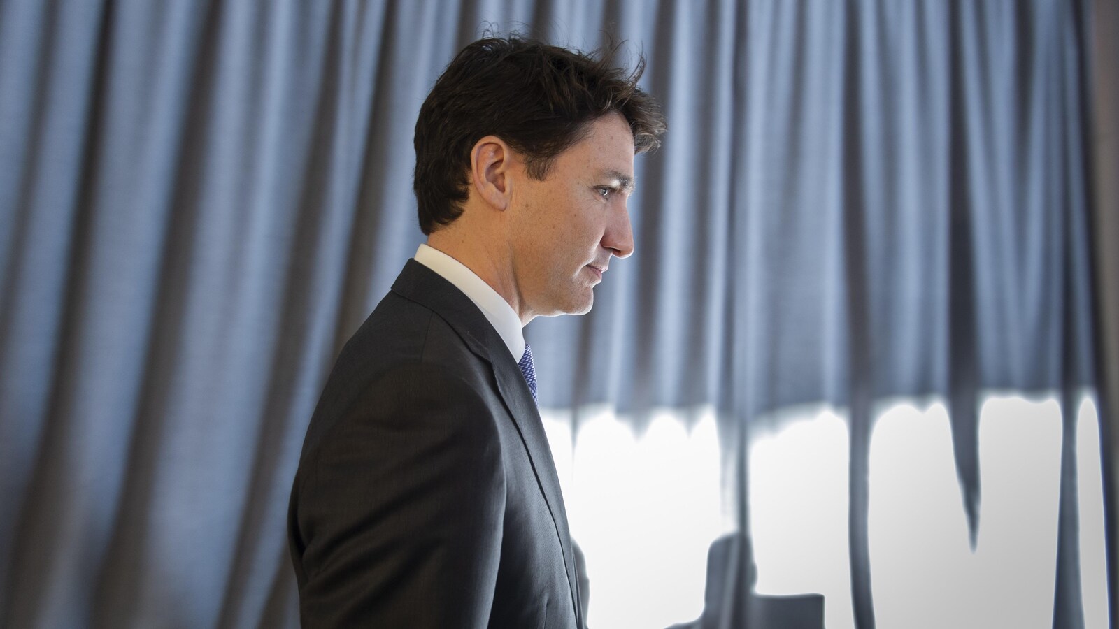 Justin Trudeau vu de côté, marchant devant un rideau.