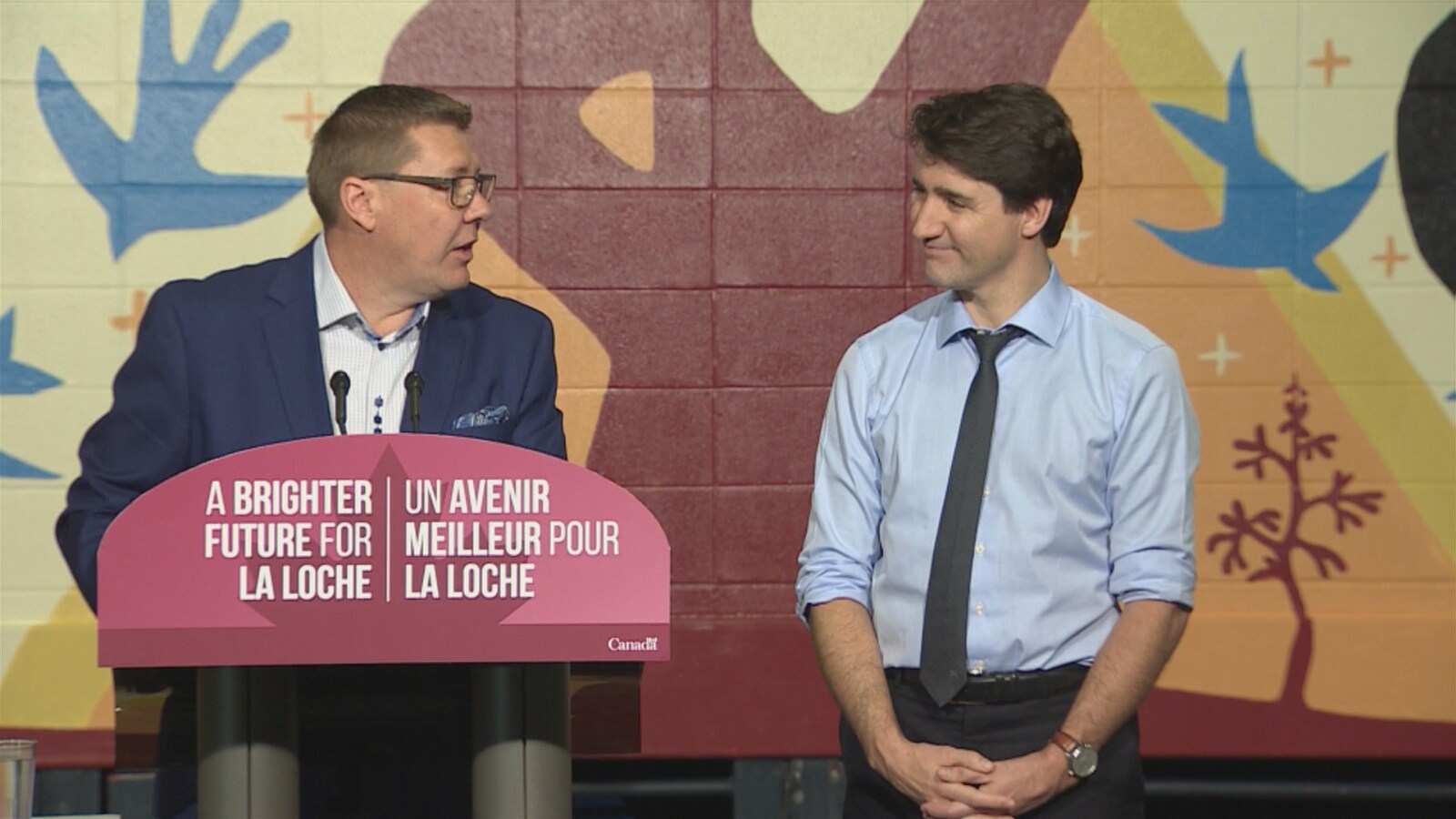 Scott Moe prend la parole avec Justin Trudeau à son côté. En avant du pupitre on peut lire: Un avenir meilleur pour La Loche en français et en anglais.