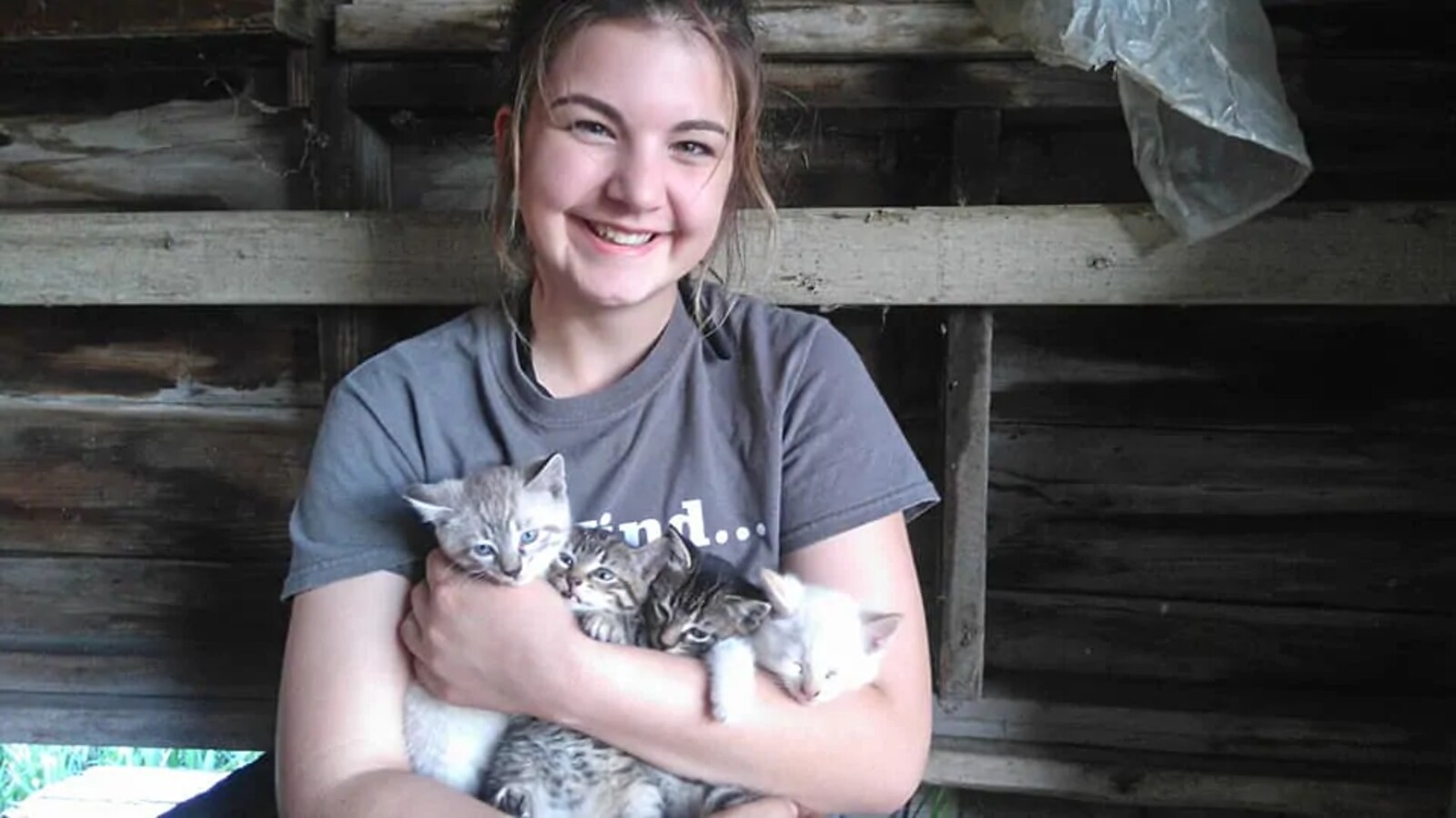 Une jeune femme assise dans une grange en bois tient quatre chatons dans ses bras.