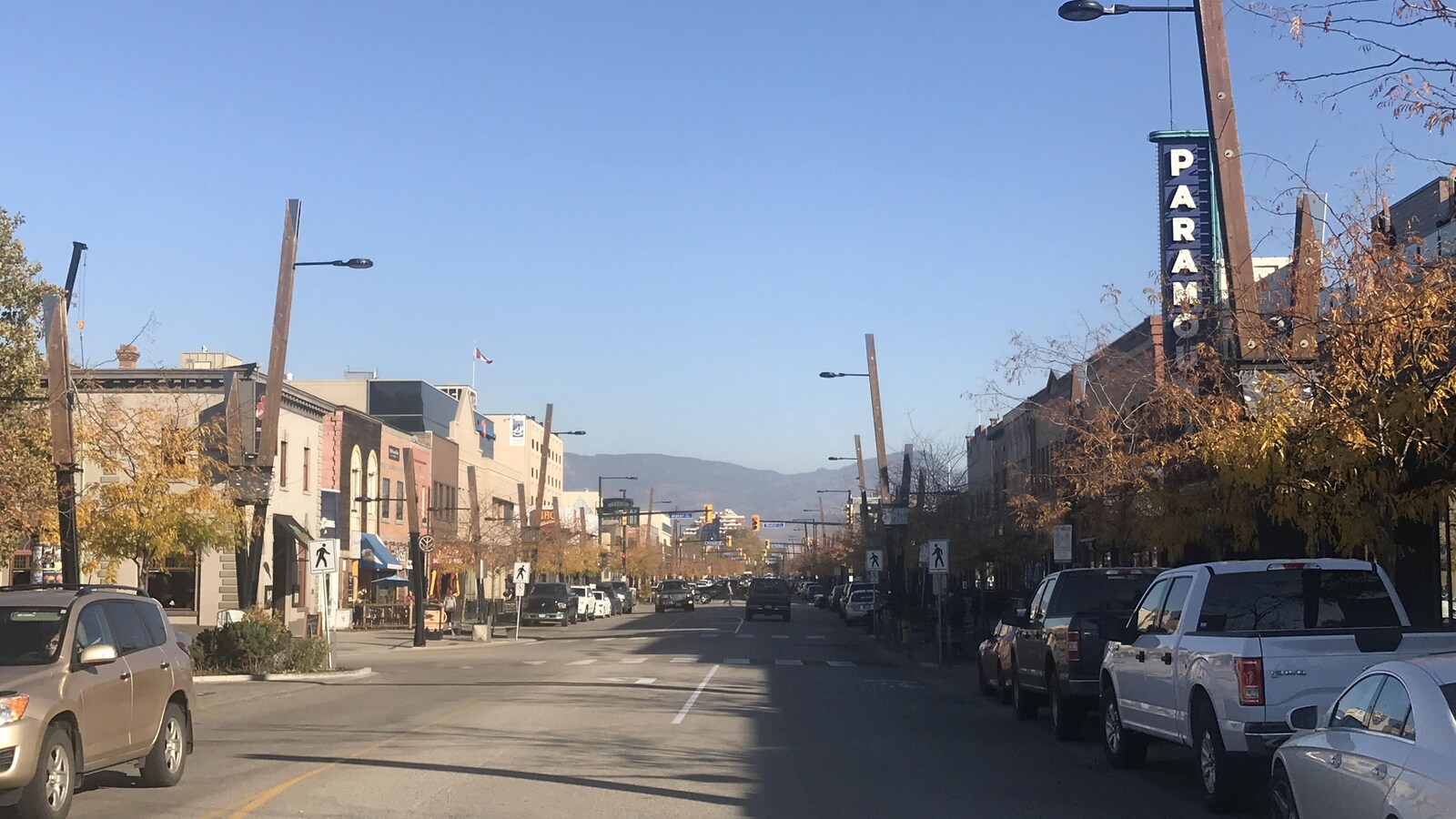 Une rue avec des voitures qui roulent et d'autres qui sont garées, et les montagnes au loin.