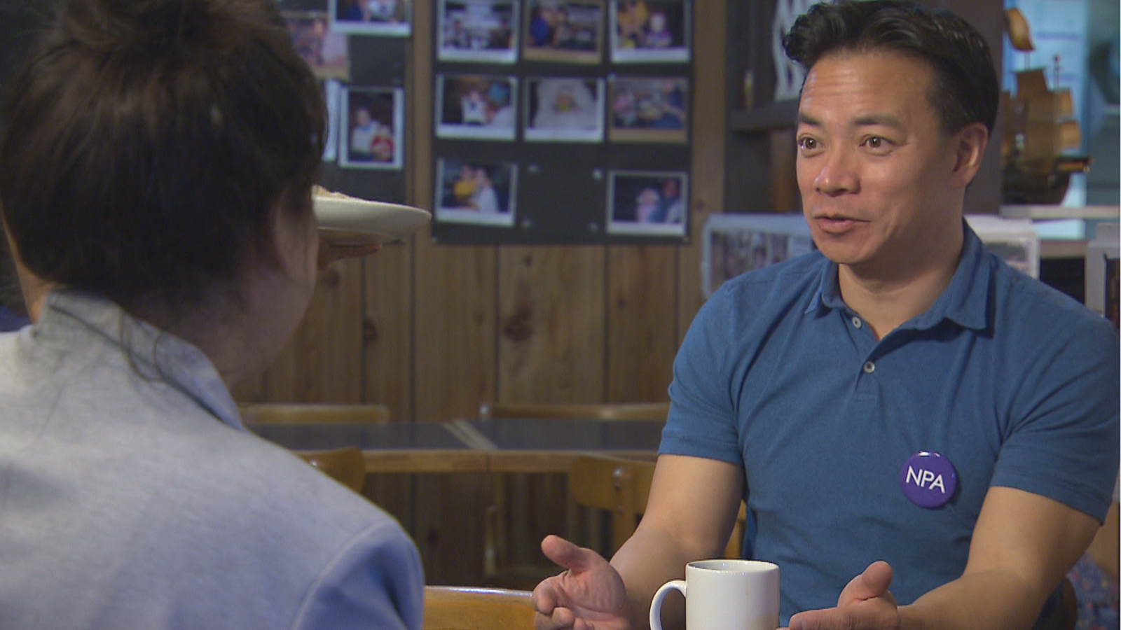 Ken Sim parle à la journaliste avec une tasse de café devant lui.