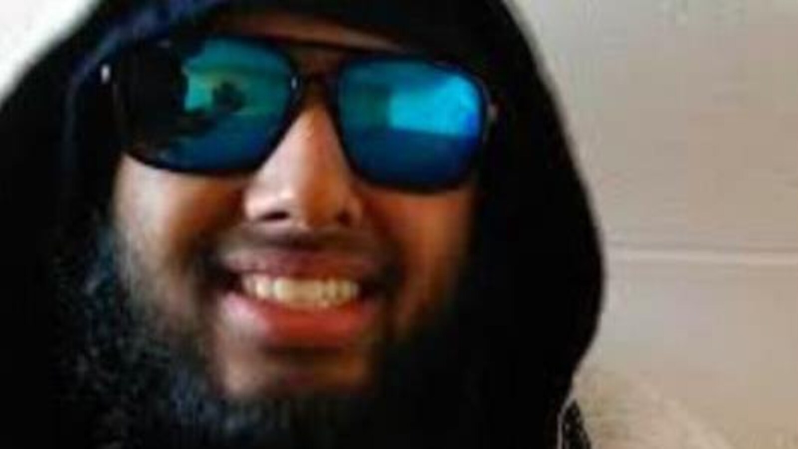 Un homme souriant portant barbe et lunettes fumées