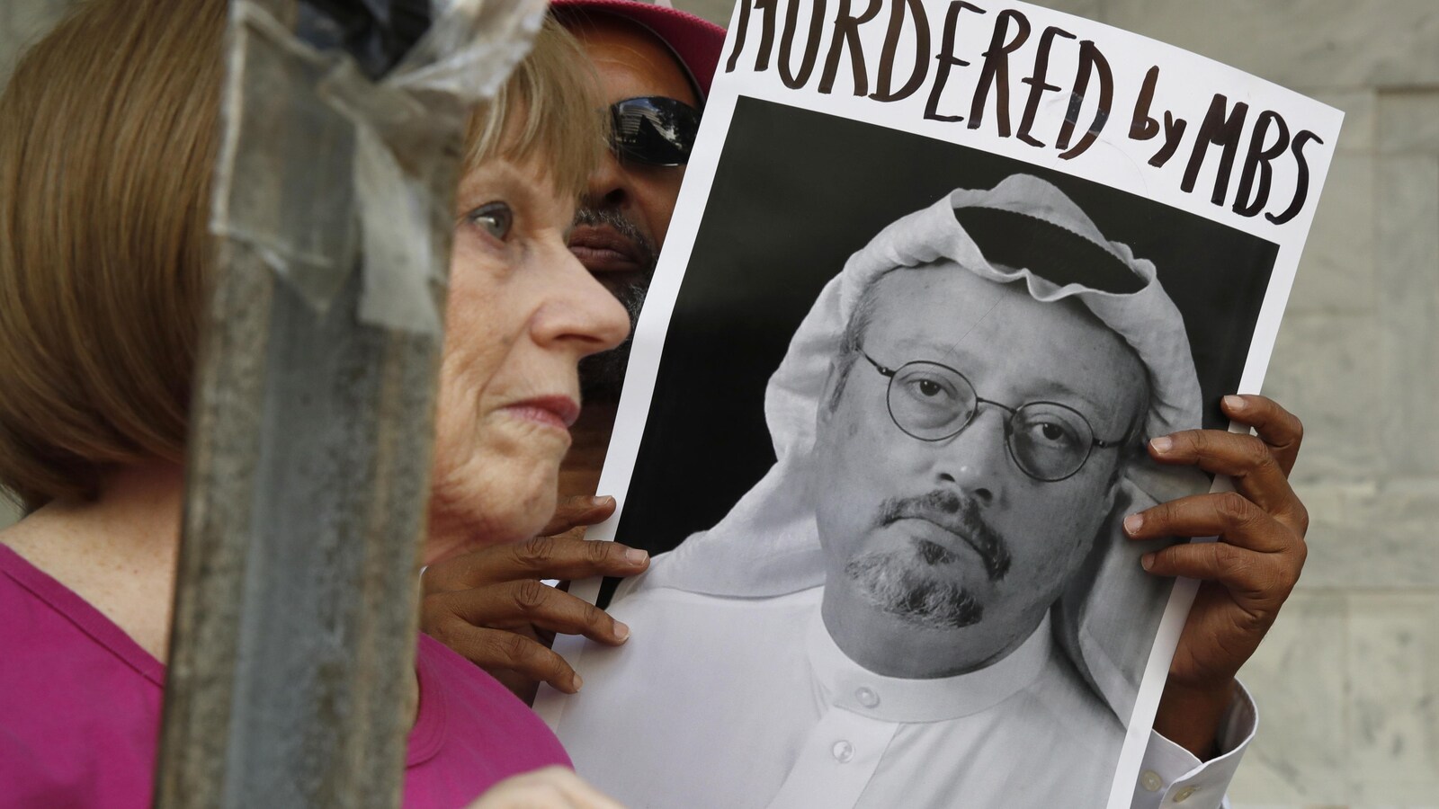 Une pancarte avec la photo du journaliste saoudien Jamal Khashoggi est entre les mains d'un manifestant, qui est aux côtés d'une femme à l'air pensif.