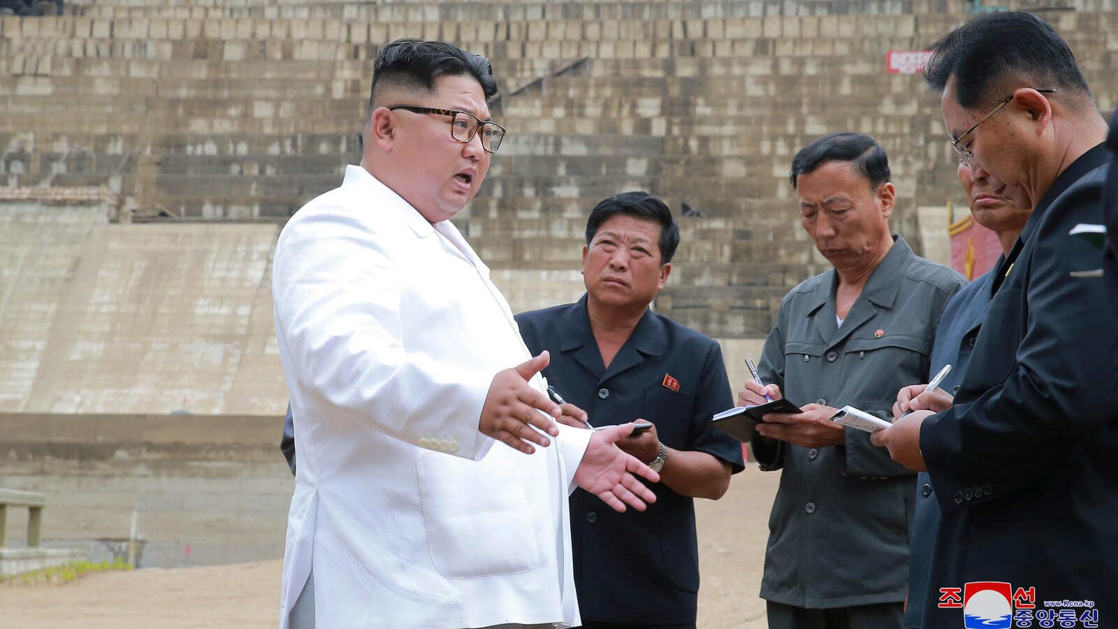 Un Asiatique s'adresse à d'autres hommes, l'air sérieux. Les autres hommes prennent des notes sur des calepins.