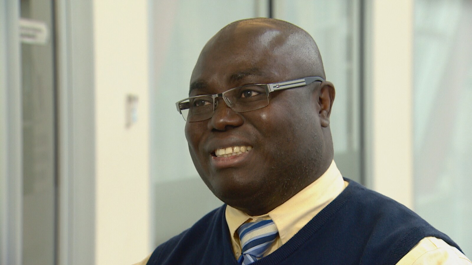 Kouamé Adie est un homme noir, chauve, avec des lunettes. Il sourit.