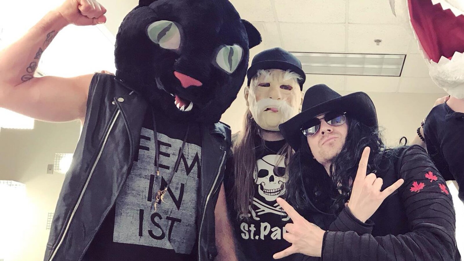 Quatre hommes costumés prennent la pause, l'un d'entre porte une tête de chat en peluche et un débardeur imprimé du mot de «feminist». Il lève le bras en serrant le poing.