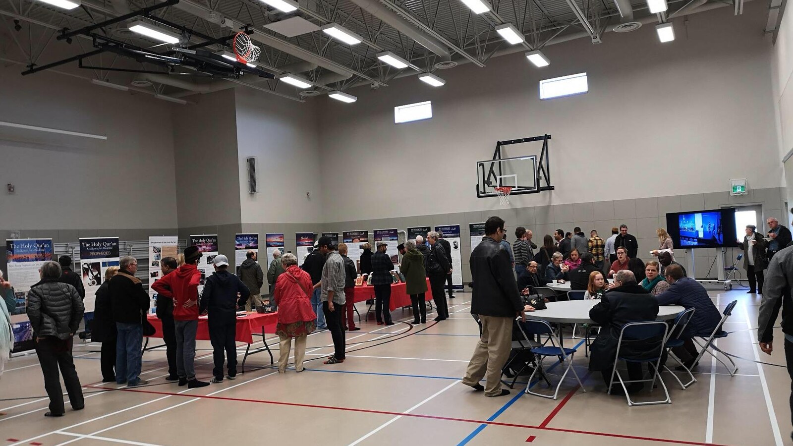 Des personnes visitent des tables d’exposition et regardent des affiches dans un gymnase lors de la journée portes ouvertes de la mosquée Baitur Rahmat de Saskatoon .