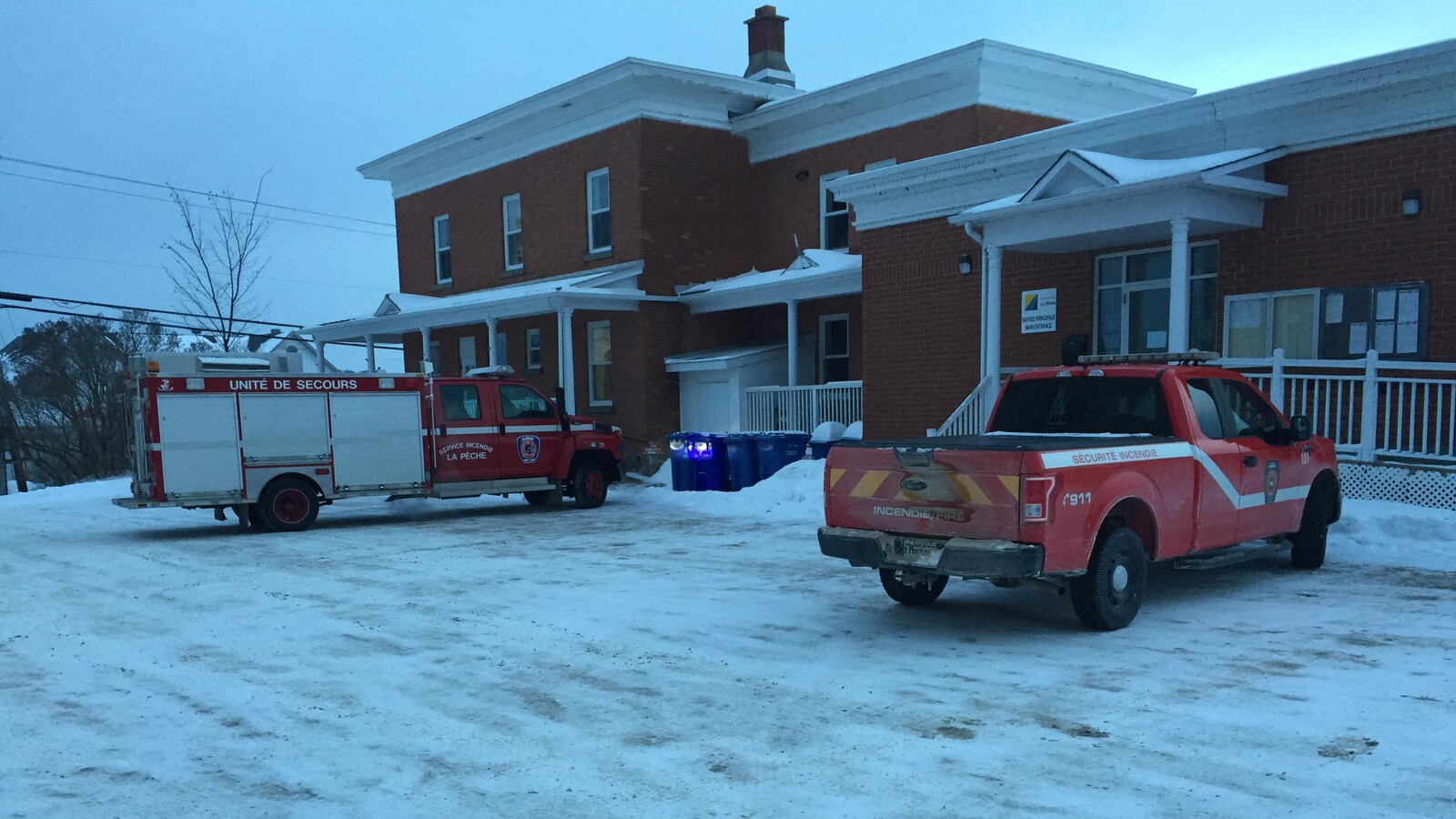 Deux camions du service incendie de La Pêche stationnés devant un édifice en hiver.