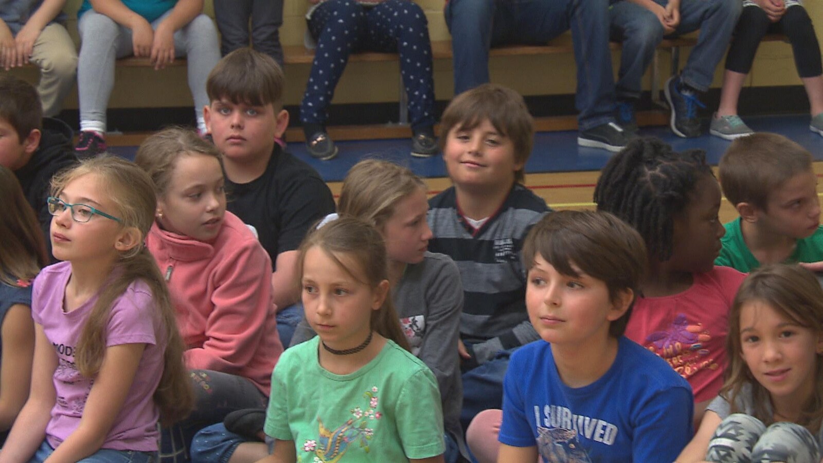 Des enfants sagement assis sur le sol d'un gymnase.