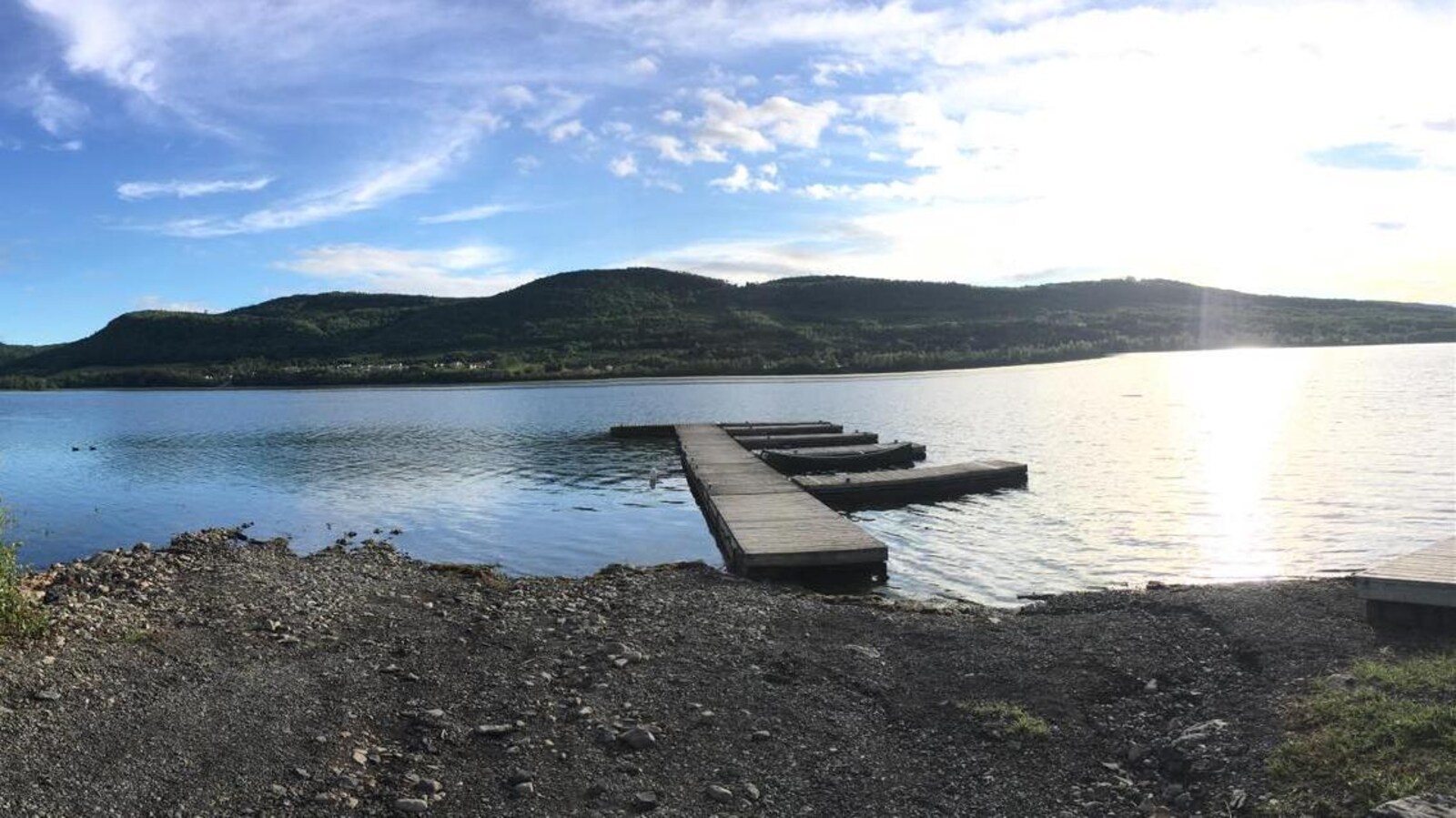 Un quai flotte sur l'eau du lac. De l'autre côté, on peut voir des collines verdoyantes.