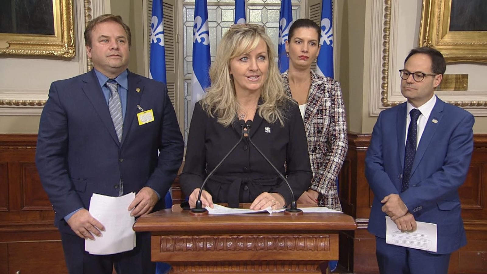 Mme Laforest, au podium, est entourée de deux hommes. La ministre Guilbault se trouve derrière elle.