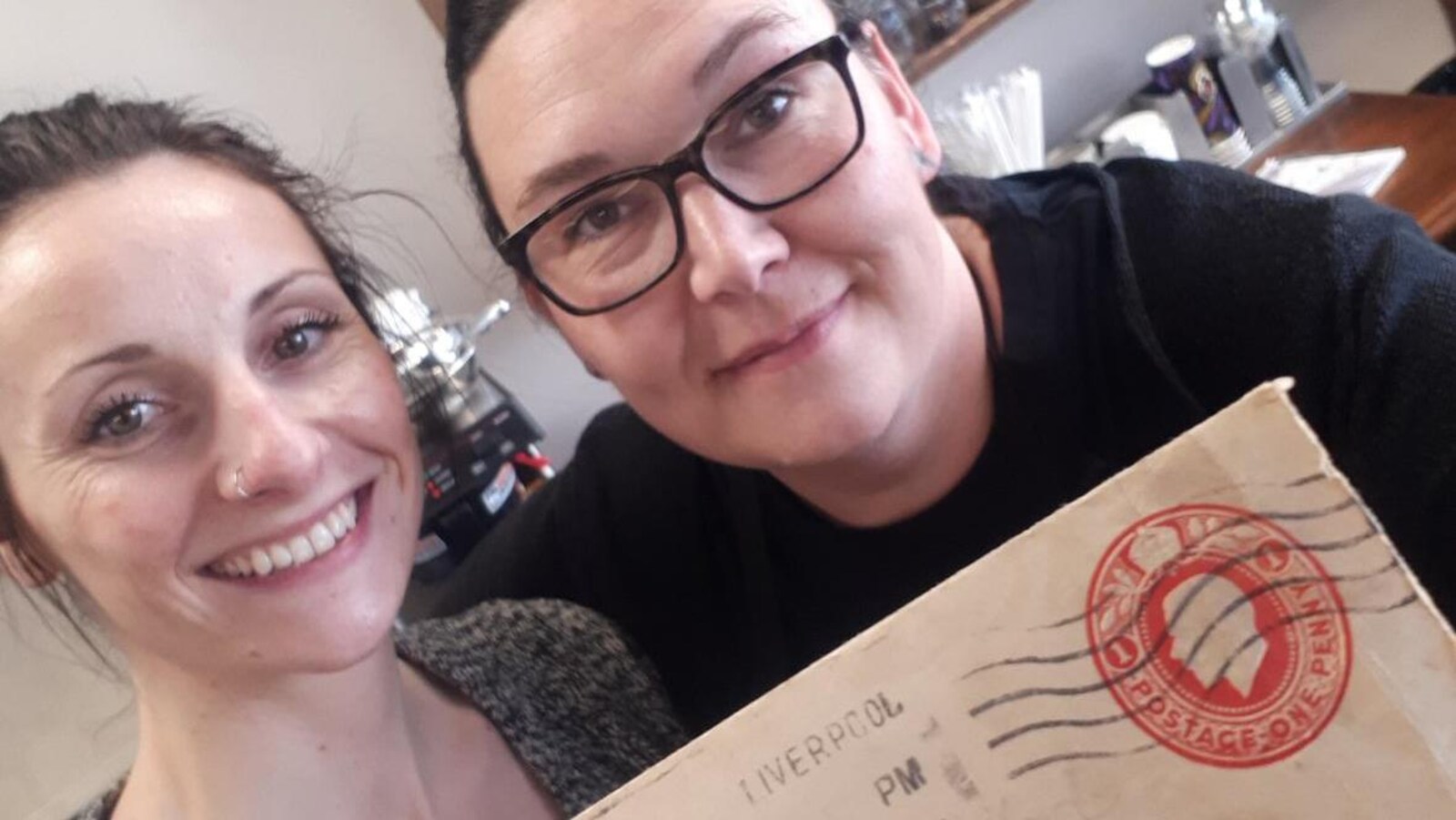 Deux femmes posent avec une lettre dans un café.