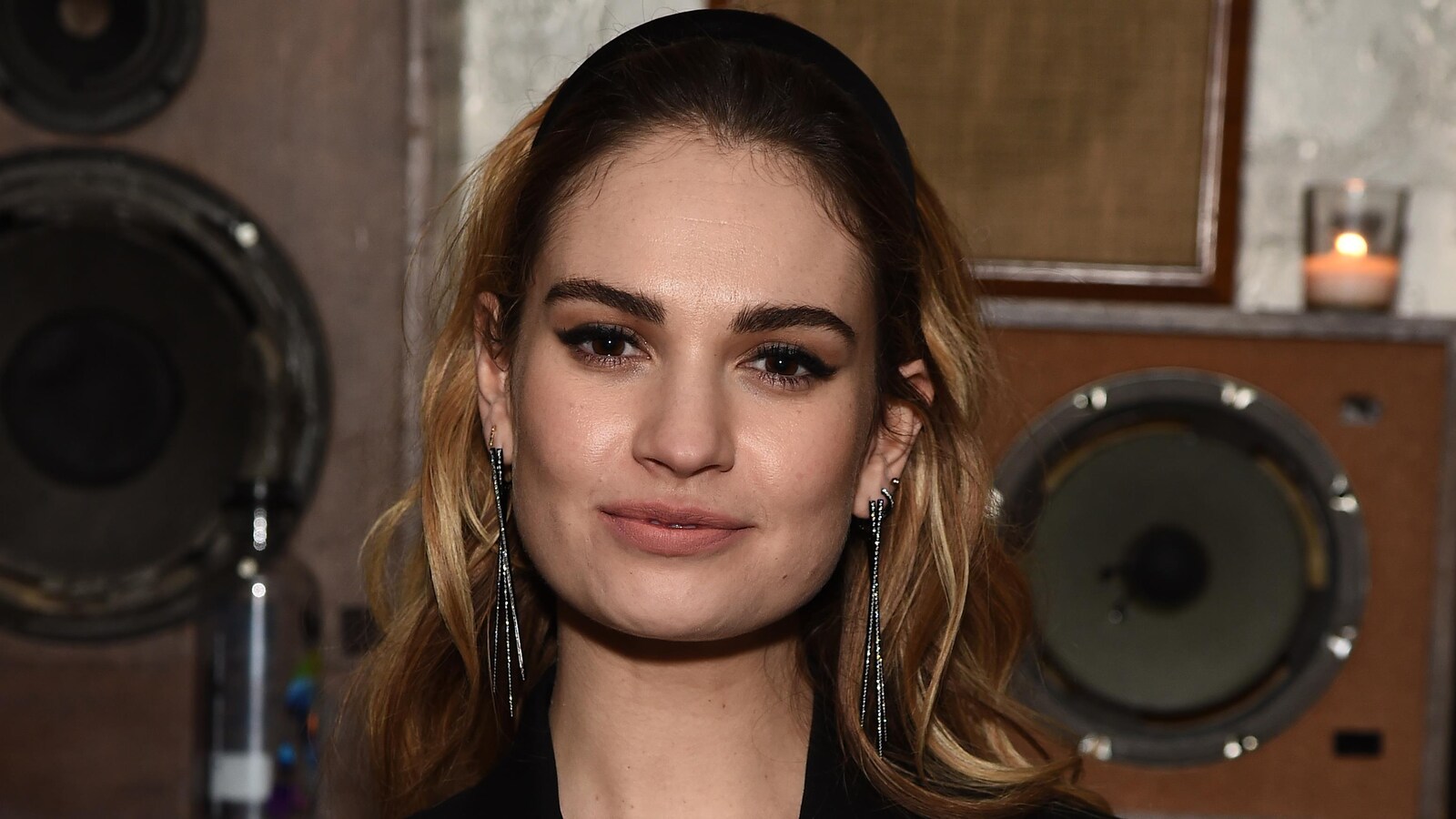 L'actrice Lily James regarde l'objectif et sourit. En arrière, on distingue des enceintes.