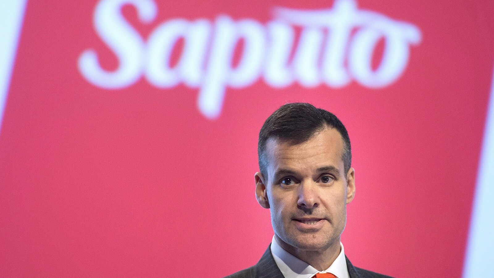 Lino Saputo fils devant un mur rouge et le logo de la compagnie Saputo.