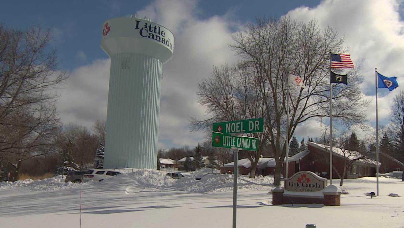 Une tour d'eau et un panneau près d'un drapeau américain aux abords d'une route enneigée portent la mention Little Canada et le logo d'une feuille d'érable.