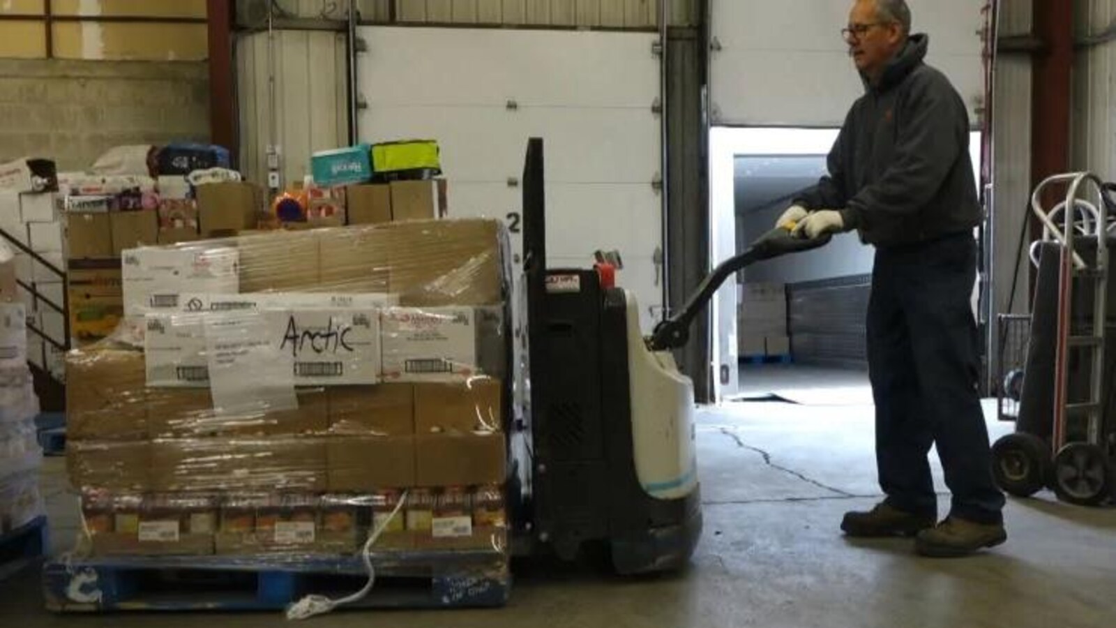 Un homme dans un hangar pousse des boîtes entassées sur lesquelles ont peut lire « Arctic »