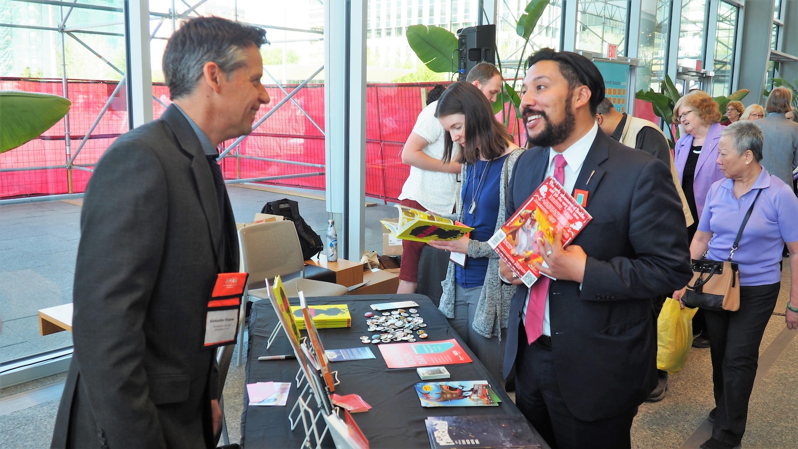 Un éditeur discute avec le ministre de la Culture et du Tourisme, Ricardo Miranda. Le ministre tient un magazine dans la main. Derrière lui, une foule regarde les stands de livres.