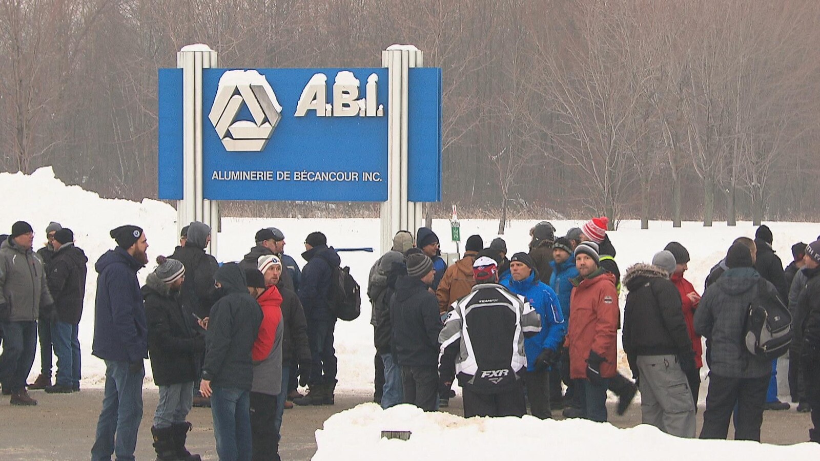 Gens rassemblés en face de l'aluminerie l'hiver, près de la pancarte ABI extérieure