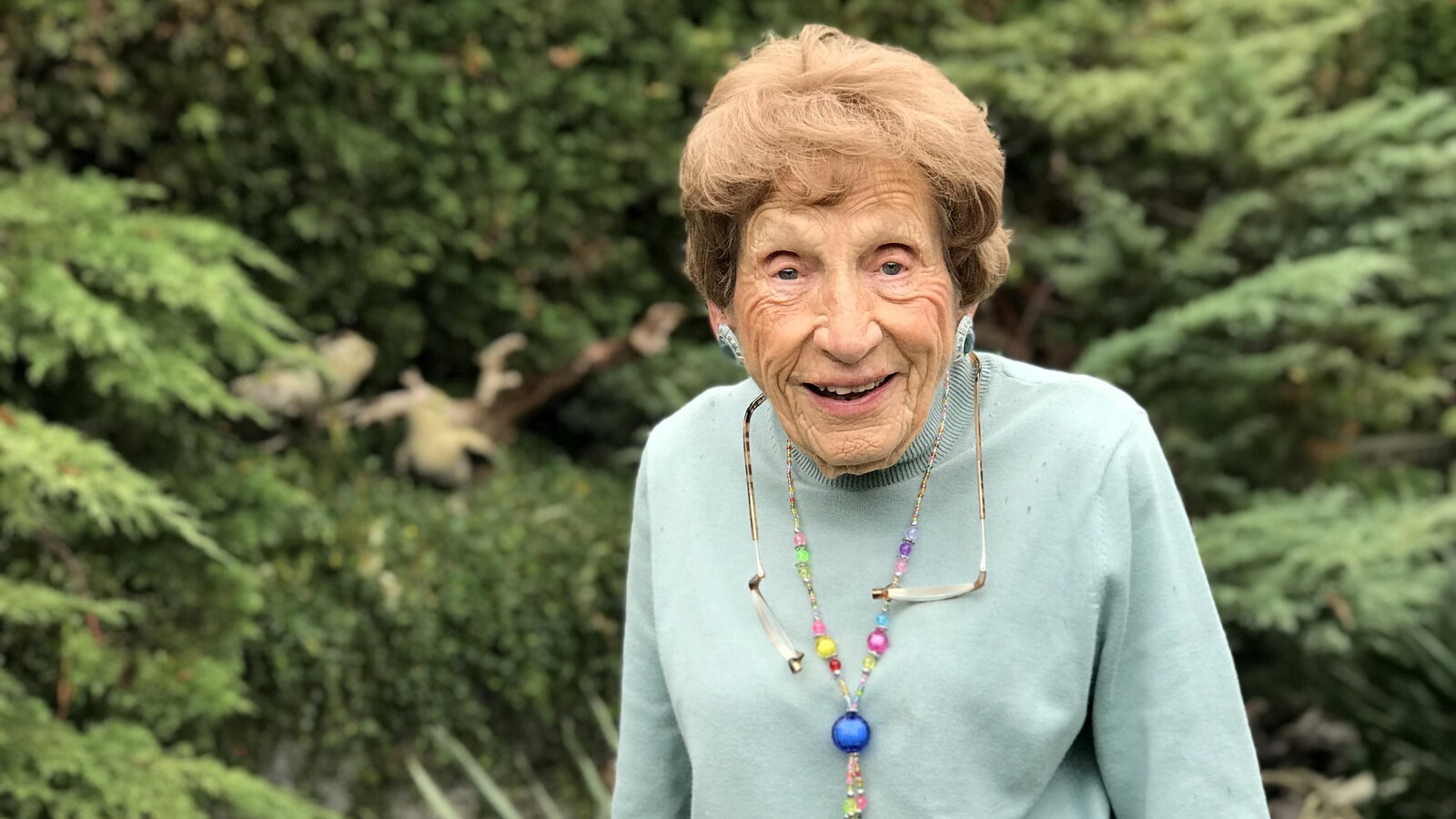 Une femme âgée qui sourit. Elle porte un col roulé vert pâle.