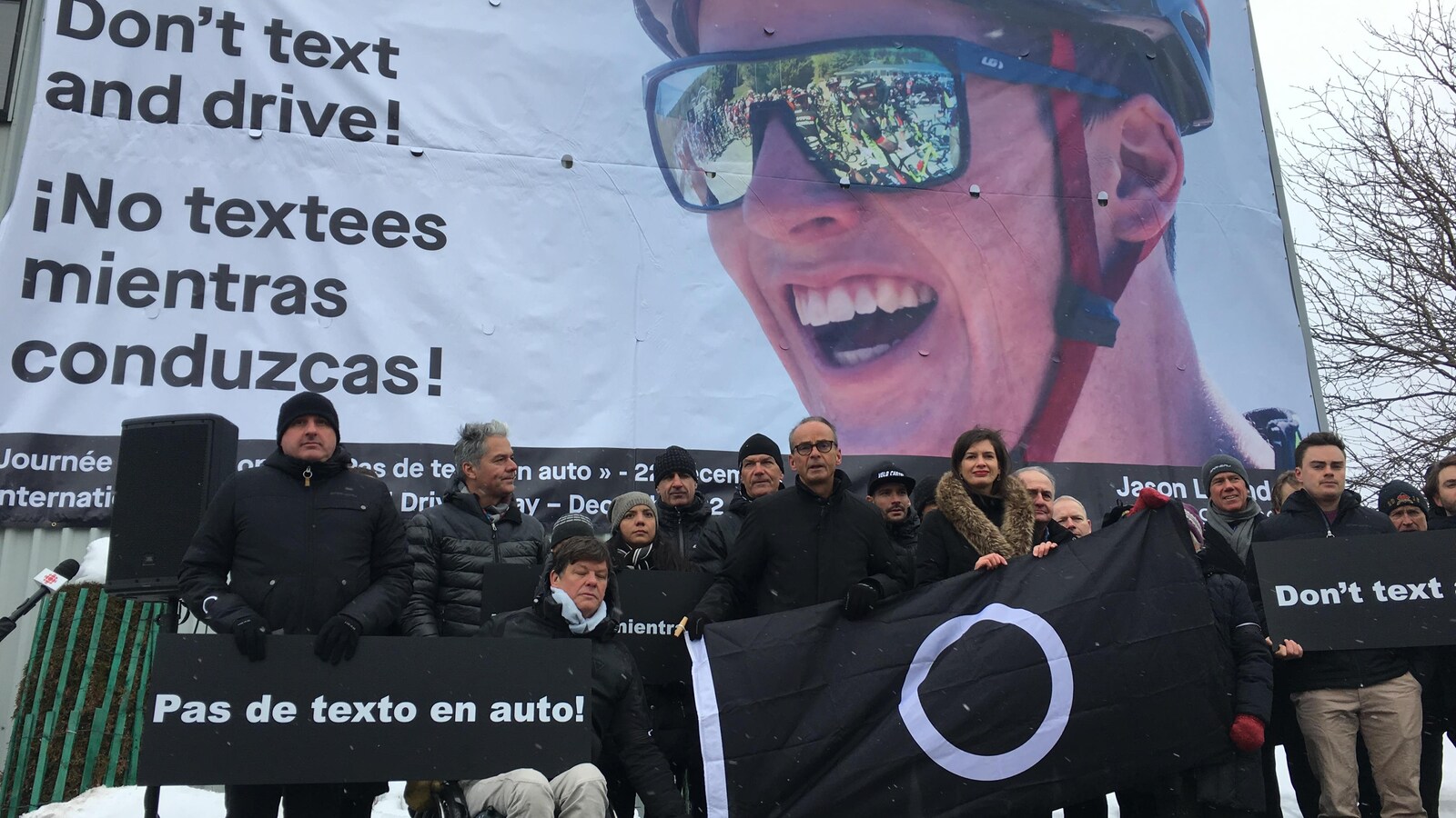 Louis Garneau entouré de plusieurs personnes éprouvées par le décès d'un proche happé mortellement par un automobiliste distrait. Sur l'affiche en arrière-plan, Jason Lowndes, mort le 22 décembre 2017.