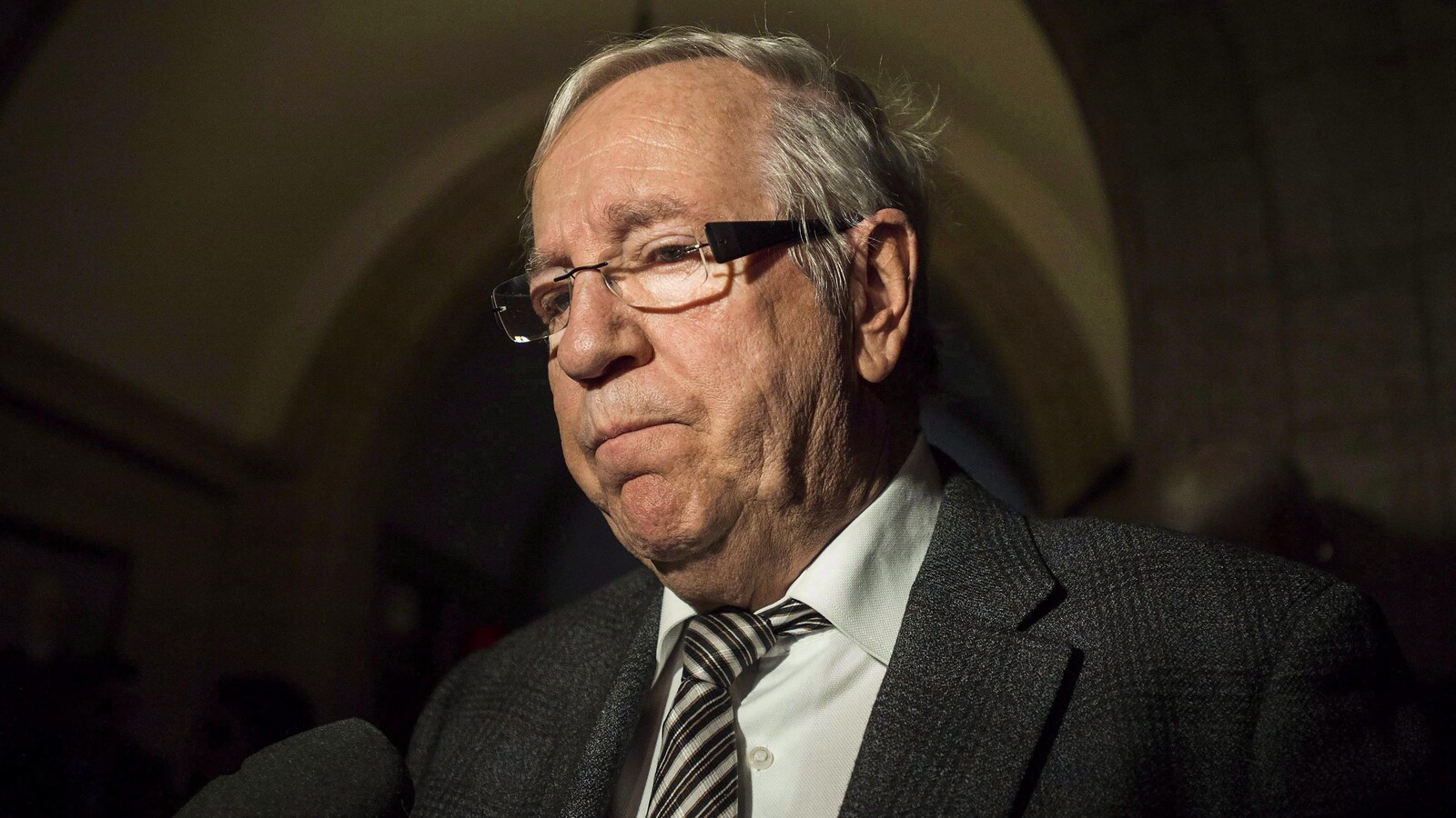 Un homme portant un complet et une cravate est interrogé par un journaliste dans un corridor du Parlement à Ottawa.
