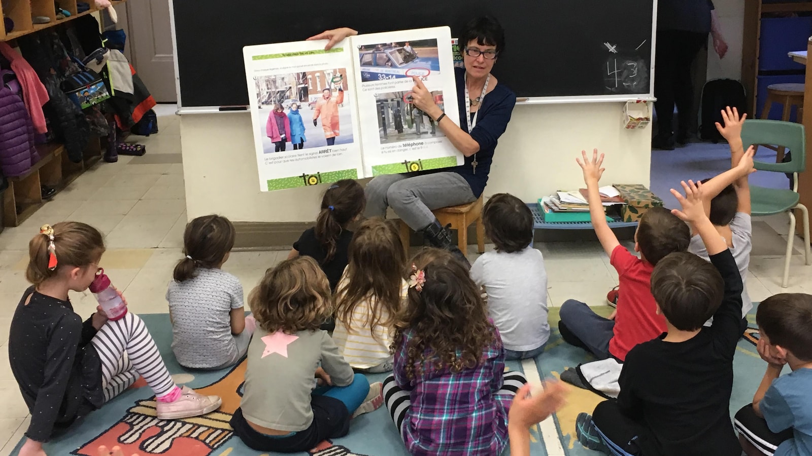 Des enfants assis par terre écoutent l'enseignante.