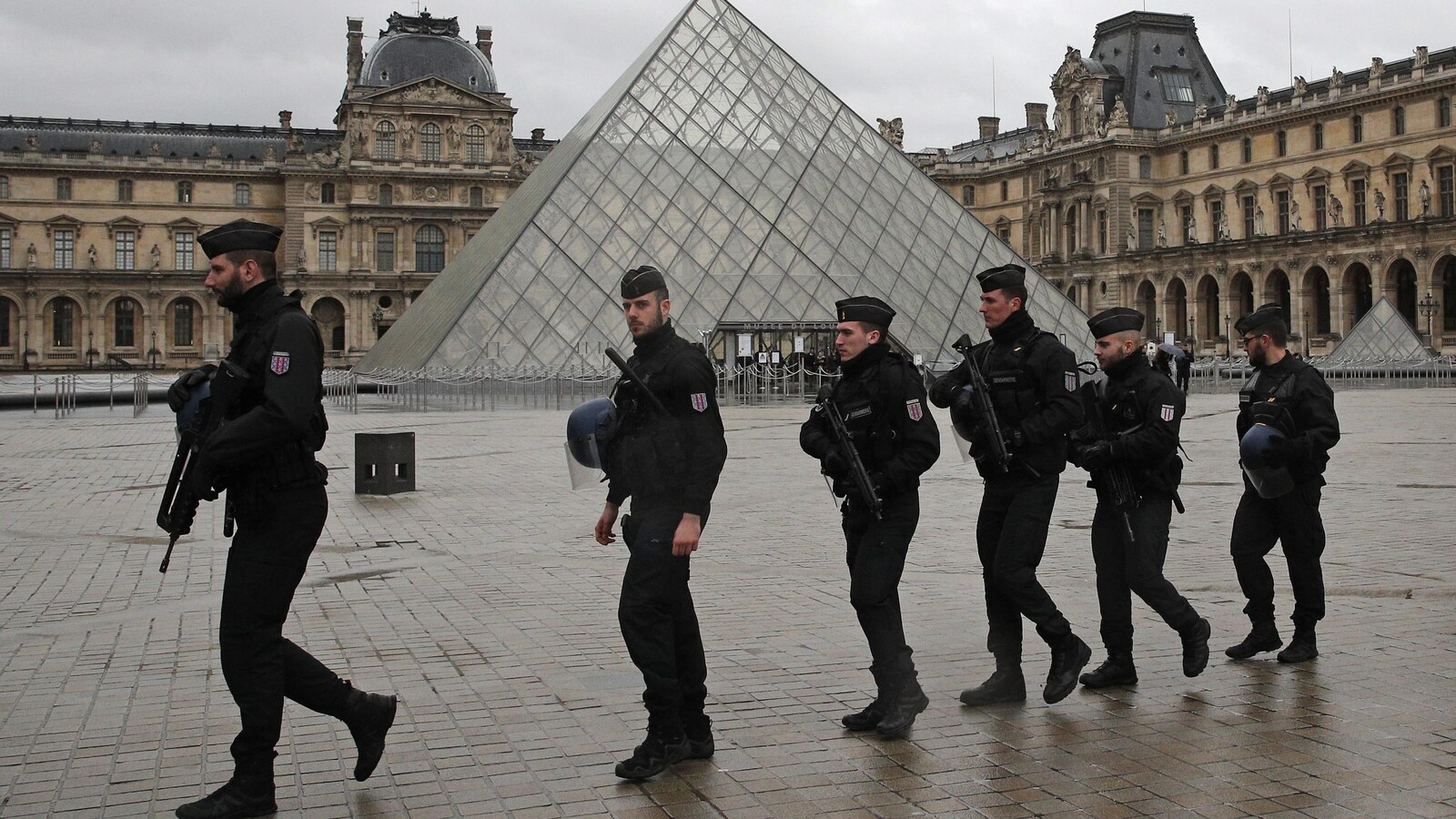 Six soldats marchent en file sur les lieux de l'attaque, au Louvre.